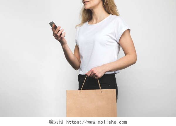 白色背景上手提购物袋的女士在白色的空白 t恤衫上的妇女的裁剪拍摄的购物袋和智能手机